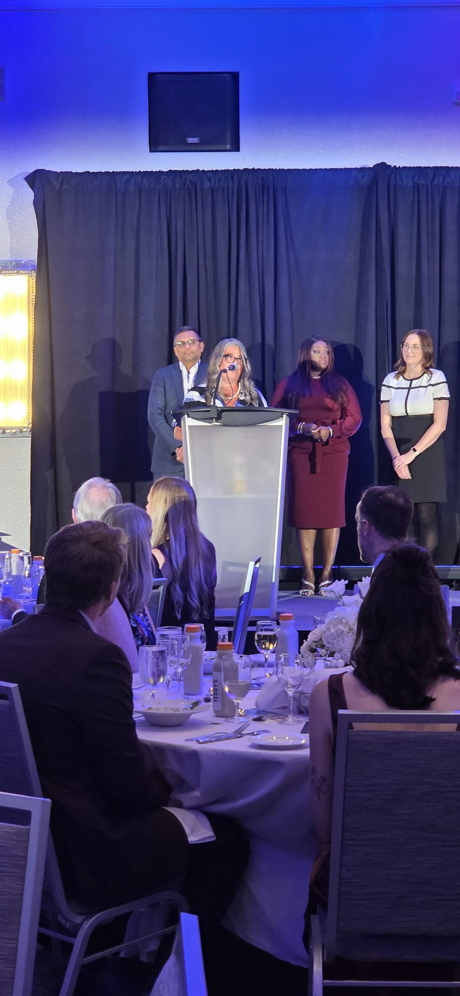 Stacey Lepine-Fisher speaking at a podium during a community awards dinner.